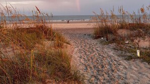 Une plage où l’on peut apercevoir un arc-en-ciel, avec un sol sablonneux et une végétation clairsemée.