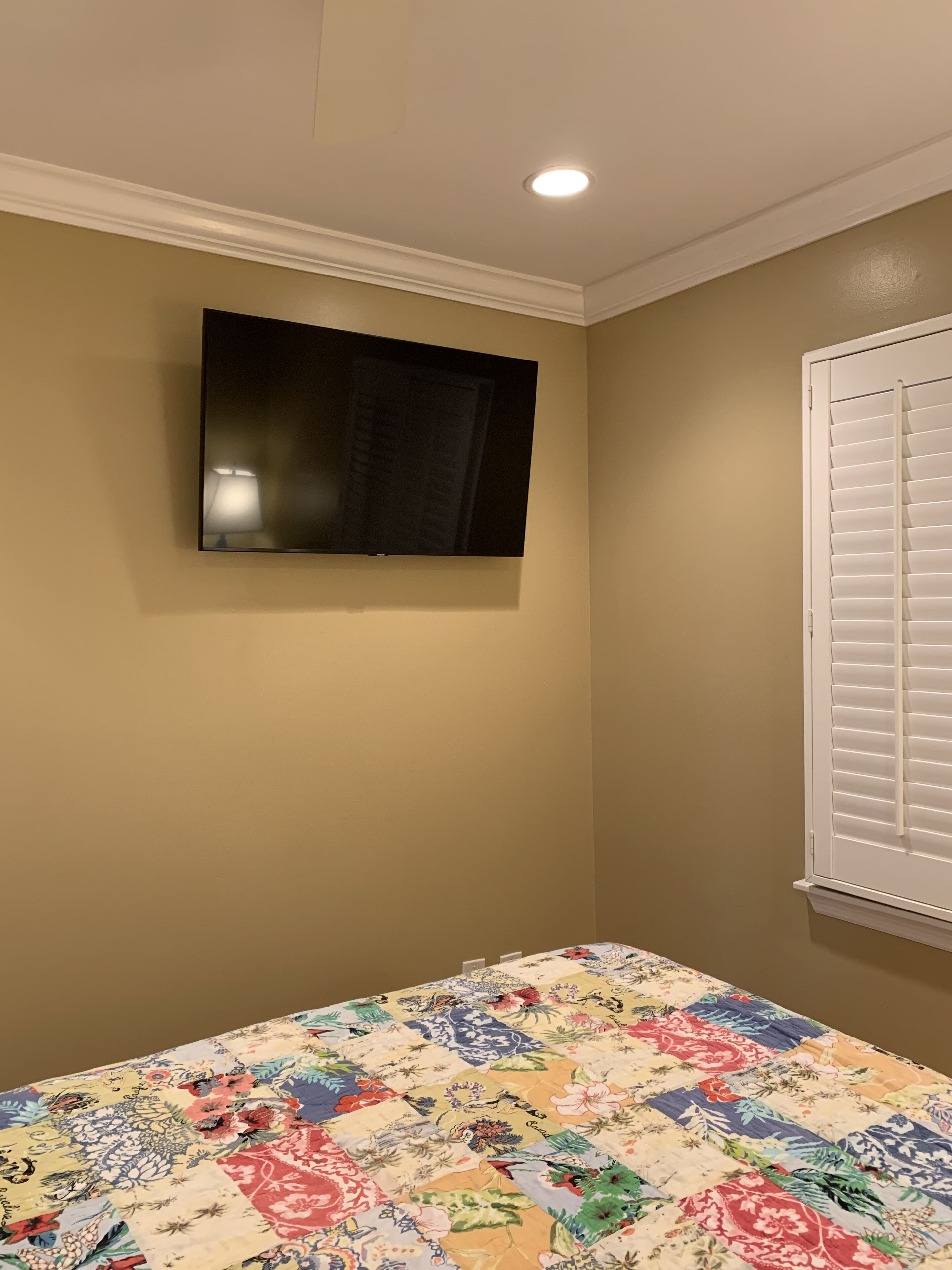 Une chambre à coucher avec un lit, un téléviseur fixé au mur et une fenêtre avec des stores.