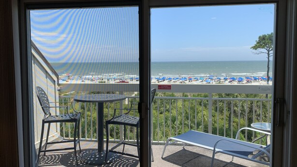 Un balcon avec vue sur la plage, une table, deux chaises et un transat.