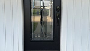 A black front door with a glass panel, two wall-mounted lanterns, and a welcome mat. - Peaceful Retreat for Families/Couples/Groups - All Sports Lake w/ Kayaks & SUP's (Cadillac)