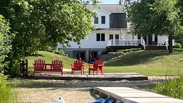 A lakeside property with a dock, red Adirondack chairs, and a kayak. - Peaceful Retreat for Families/Couples/Groups - All Sports Lake w/ Kayaks & SUP's (Cadillac)