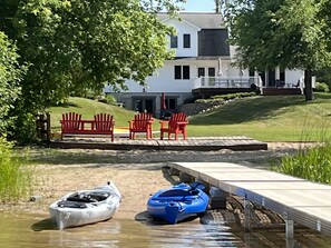 En fastighet vid sjön med en brygga, röda Adirondack-stolar och en kajak.