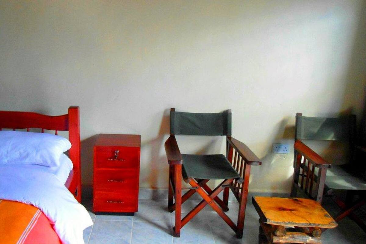 Una habitación con una cama, una mesita de noche roja, dos sillas de madera y una pequeña mesa.