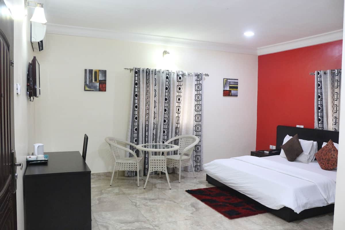 A hotel room with a bed, a desk, two chairs, a red accent wall, and curtains.