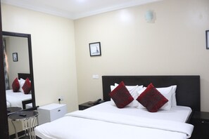 Une chambre d’hôtel comprenant un lit, une table de chevet, un petit bureau, une chaise et un miroir.