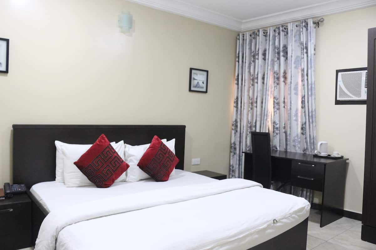 A hotel room with a bed, a desk, a chair, and a window with curtains.