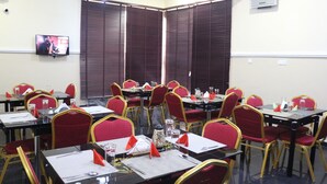A conference room with tables and chairs, a television on the wall, and a window with blinds.