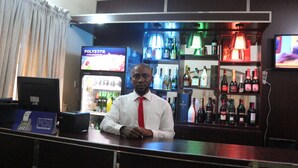 A bar area with a bartender, a POS terminal, and shelves stocked with various bottles.