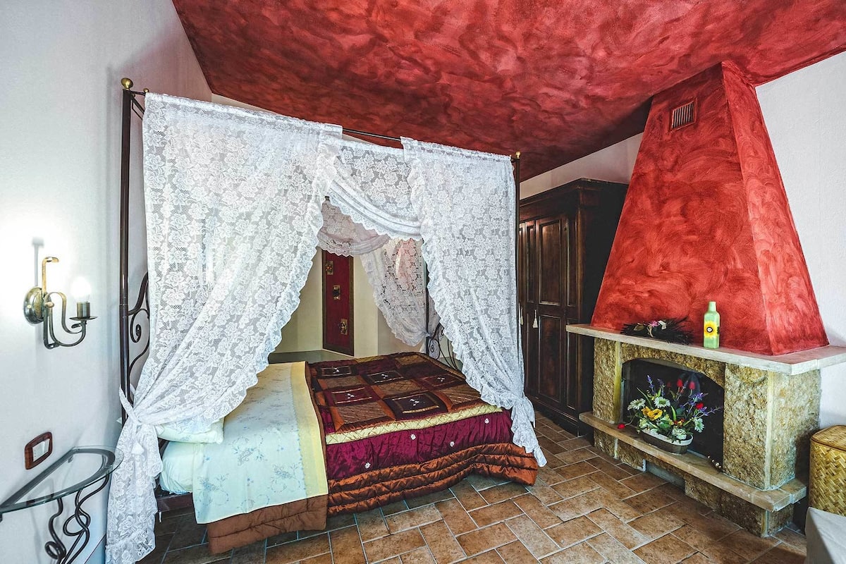 Ein Schlafzimmer mit Himmelbett, Kamin und roter Decke.
