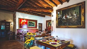 A dining area with wooden tables set for a meal, surrounded by framed artwork and a rustic ceiling. - Agriturismo Palazzo Conti A (San Quirico d'Orcia)