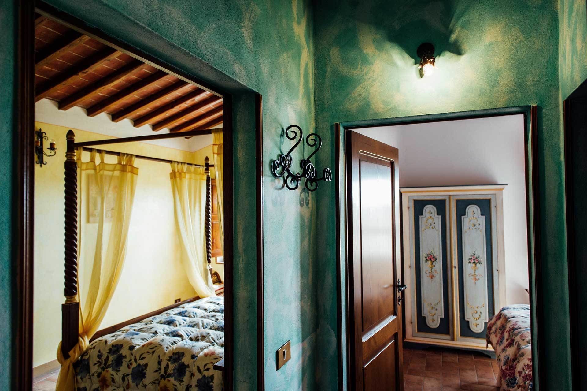 A bedroom with a canopy bed, a wall-mounted light fixture, and a door leading to another room with a wardrobe.