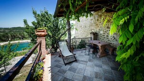 A stone patio with a swing chair, a table, and a view of a body of water. - Agriturismo Palazzo Conti A (San Quirico d'Orcia)