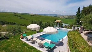 A swimming pool with lounge chairs and umbrellas, surrounded by lush greenery and a scenic view of rolling hills. - Agriturismo Palazzo Conti A (San Quirico d'Orcia)