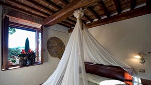 A bedroom with a canopy bed, a stone wall, and a window with a view of greenery. - Agriturismo Palazzo Conti A (San Quirico d'Orcia)