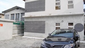 A two-story building with a car parked in front. - West 11 Luxury (Lagos)