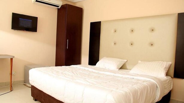 A neatly made bed with a white duvet, a dark brown headboard with tufted details, and a small bedside table. - West 11 Luxury (Lagos)