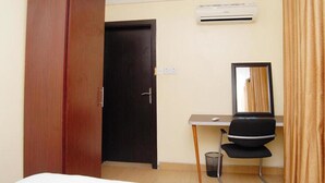 A hotel room with a wardrobe, a desk, a chair, an air conditioning unit, and a mirror. - West 11 Luxury (Lagos)