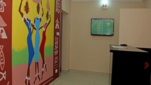 A room with a colorful mural, a television mounted on the wall, and a black podium with a red object on it. - West 11 Luxury (Lagos)