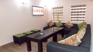 A living room with a black sofa, green cushions, a glass coffee table, and a TV on the wall. - West 11 Luxury (Lagos)