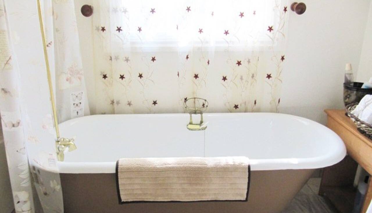 A bathroom with a freestanding bathtub, a towel rack, and a window with floral curtains.