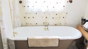 A bathroom with a freestanding bathtub, a towel rack, and a window with floral curtains.