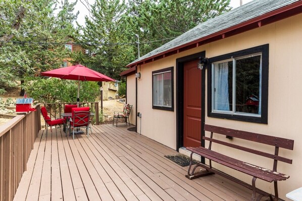 A wooden deck with a red umbrella, a bench, and a small table with chairs.