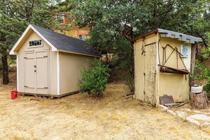 Two wooden sheds, one beige and one yellow, with a small bush in between.