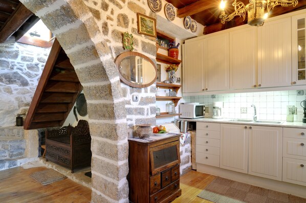 A rustic kitchen with stone walls, wooden cabinets, and a wooden chest of drawers. - Elounda Traditional Art Suites (Agios Nikolaos)