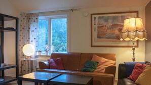A cozy living room with a brown sofa, two black tables, a colorful rug, a lamp, and a window with curtains.