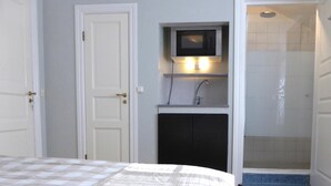 A bedroom with a bed, a small kitchenette with a microwave, and a shower area.