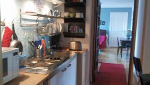 A compact kitchen with a microwave, stove, and various utensils. There is a red carpet leading to a dining area with a table and chairs.
