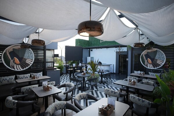 Un área de comedor al aire libre con mesas y sillas redondas, un suelo con diseño y una sombrilla grande.