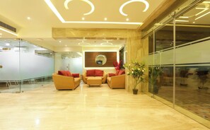 A modern lobby with a reception desk, seating area, and a large mirror. - HOTEL SRR GRAND (Chennai)
