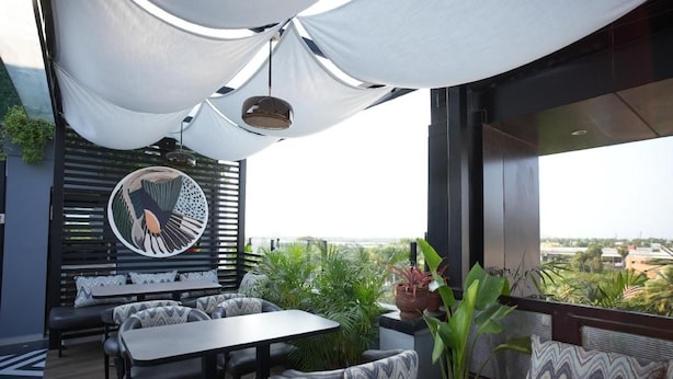 An outdoor seating area with tables and chairs, a large potted plant, and a view of the cityscape. - HOTEL SRR GRAND (Chennai)
