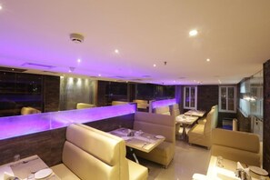 Un restaurante moderno con cabinas y mesas, iluminación ambiental y vistas de la ciudad de noche.