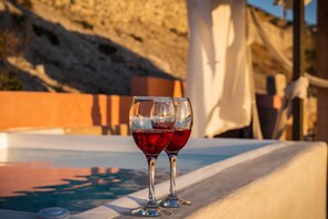 Deux verres de vin rouge sur une table au bord de la piscine, offrant une vue dégagée sur la piscine et un paysage montagneux en arrière-plan.