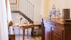 Un pasillo con suelo de cuadros, una escalera, un armario de madera y una mesa con comida y flores.