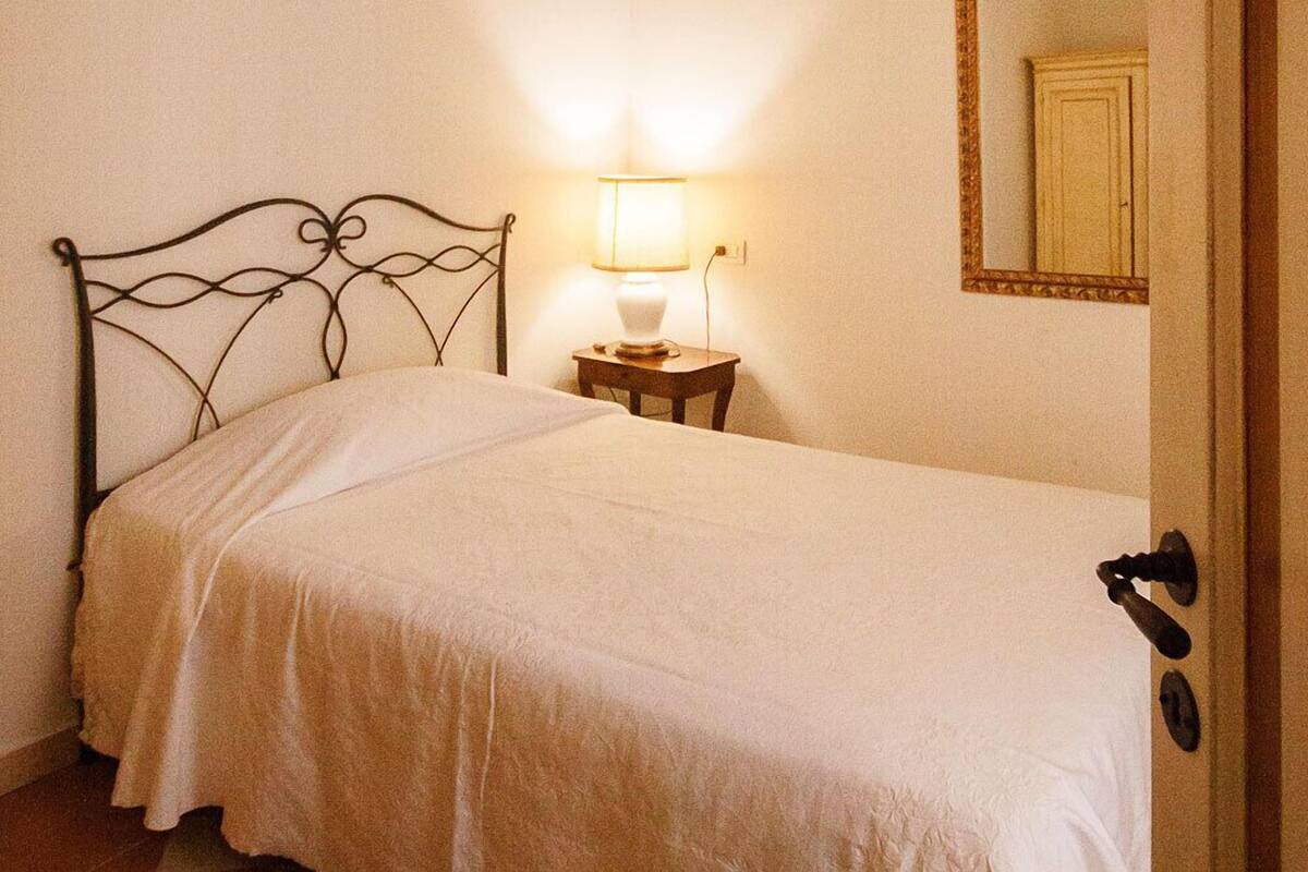 A single bed with a metal headboard, a bedside table with a lamp, and a mirror on the wall.