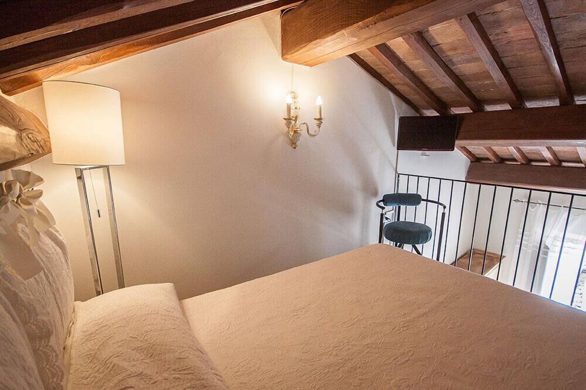 A bedroom with a bed, a bedside lamp, a wall-mounted light fixture, and a balcony railing.