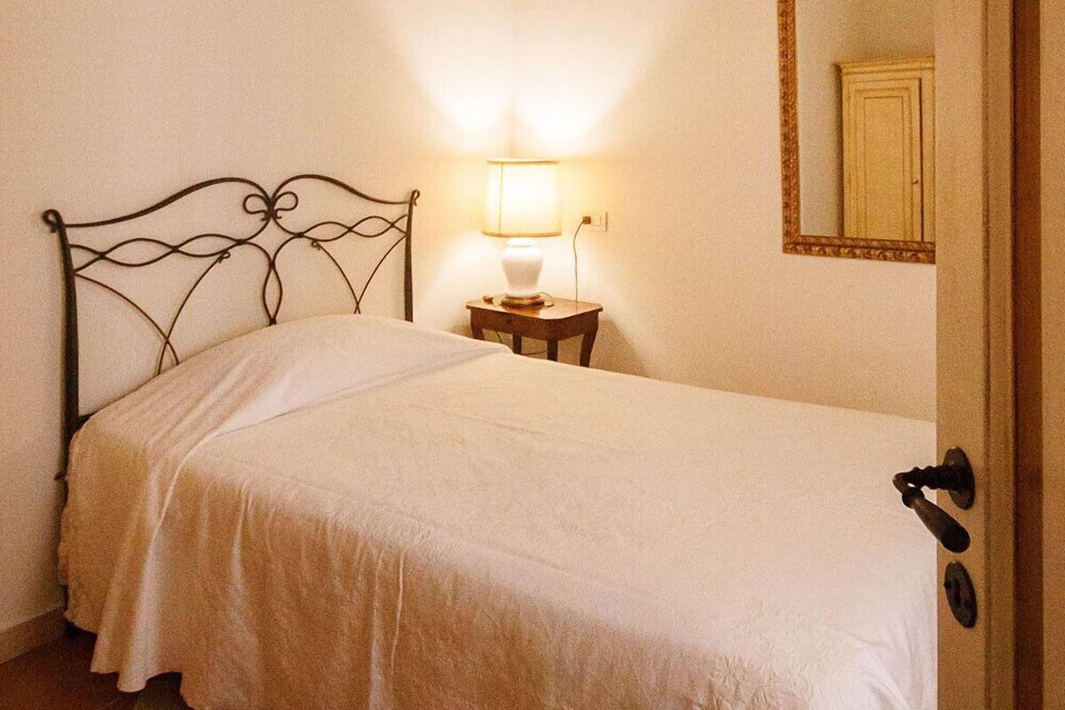 A single bed with a metal headboard, a bedside table with a lamp, and a door with a handle.