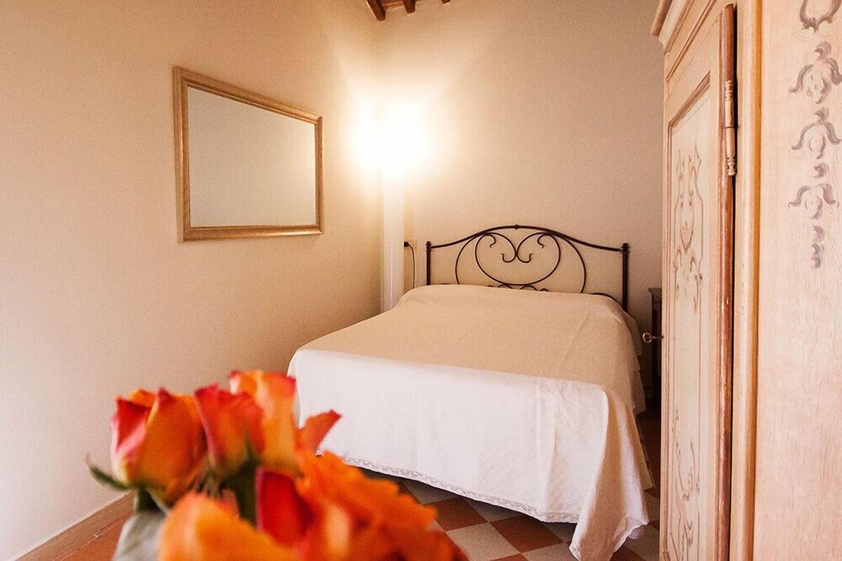 A bedroom with a bed, a bedside table, a mirror, and a door.