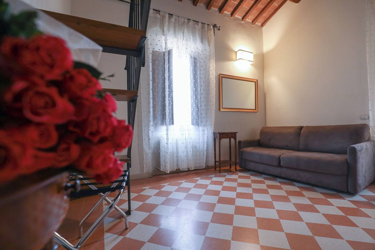 A room with a checkered floor, a sofa, a mirror, and a window with curtains.