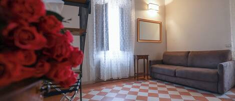 A room with a checkered floor, a sofa, a mirror, and a window with curtains.