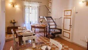 Un comedor con una mesa de madera dispuesta para dos, una escalera y un suelo a cuadros.
