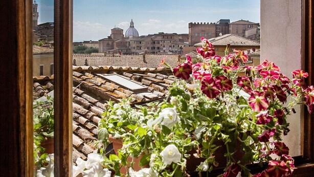 Vista desde una ventana que da a un paisaje urbano con tejados de teja y una estructura con cúpula destacada en la distancia.