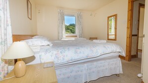 A bedroom with a bed, a bedside table with a lamp, a chair, and a window with curtains.