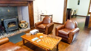 A cozy living room with a fireplace, two leather armchairs, a coffee table with chess pieces, and a bookshelf. - Le Relais du Beffroi (Saint-Riquier)