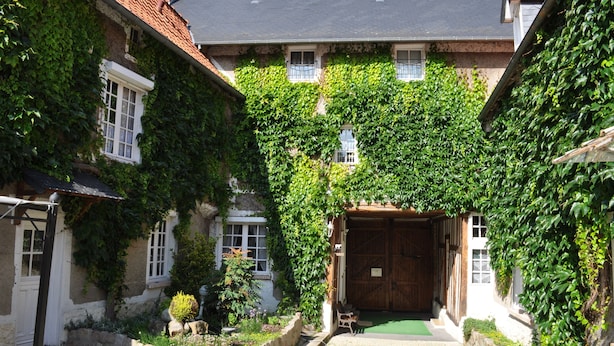 A courtyard with a central wooden door, surrounded by ivy-covered buildings with white windows and stone walls. - Le Relais du Beffroi (Saint-Riquier)