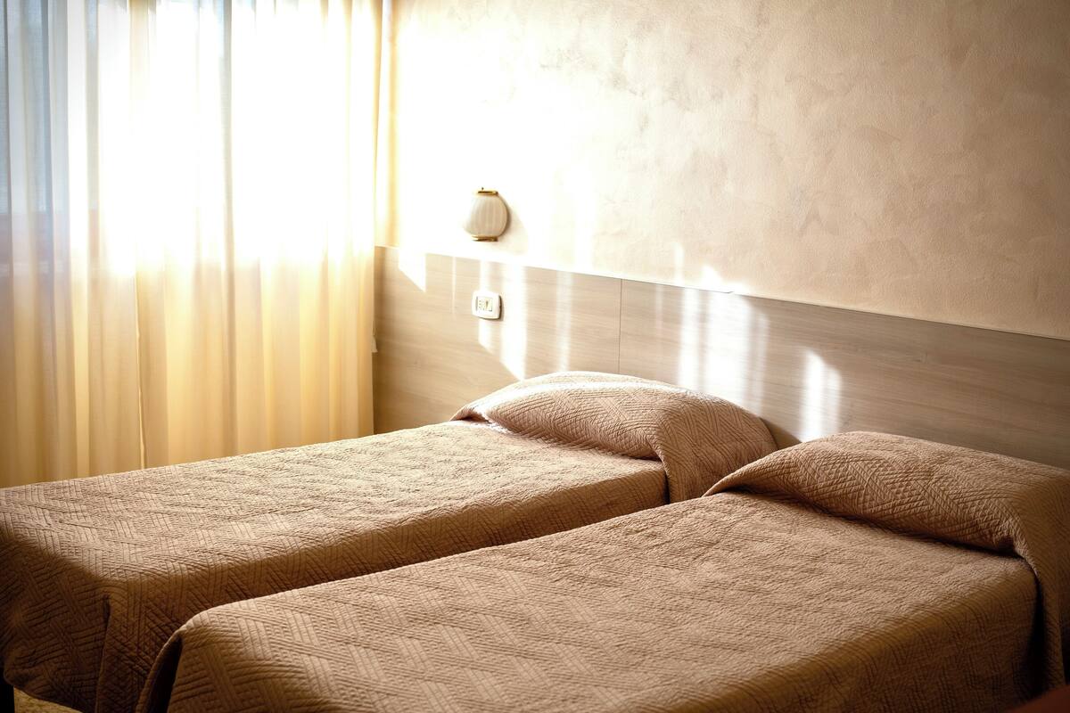 A hotel room with two beds, a wall-mounted light fixture, and a window with curtains.