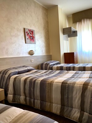 Habitación de hotel con dos camas, un cuadro de flores, una mesita y una ventana con cortinas.